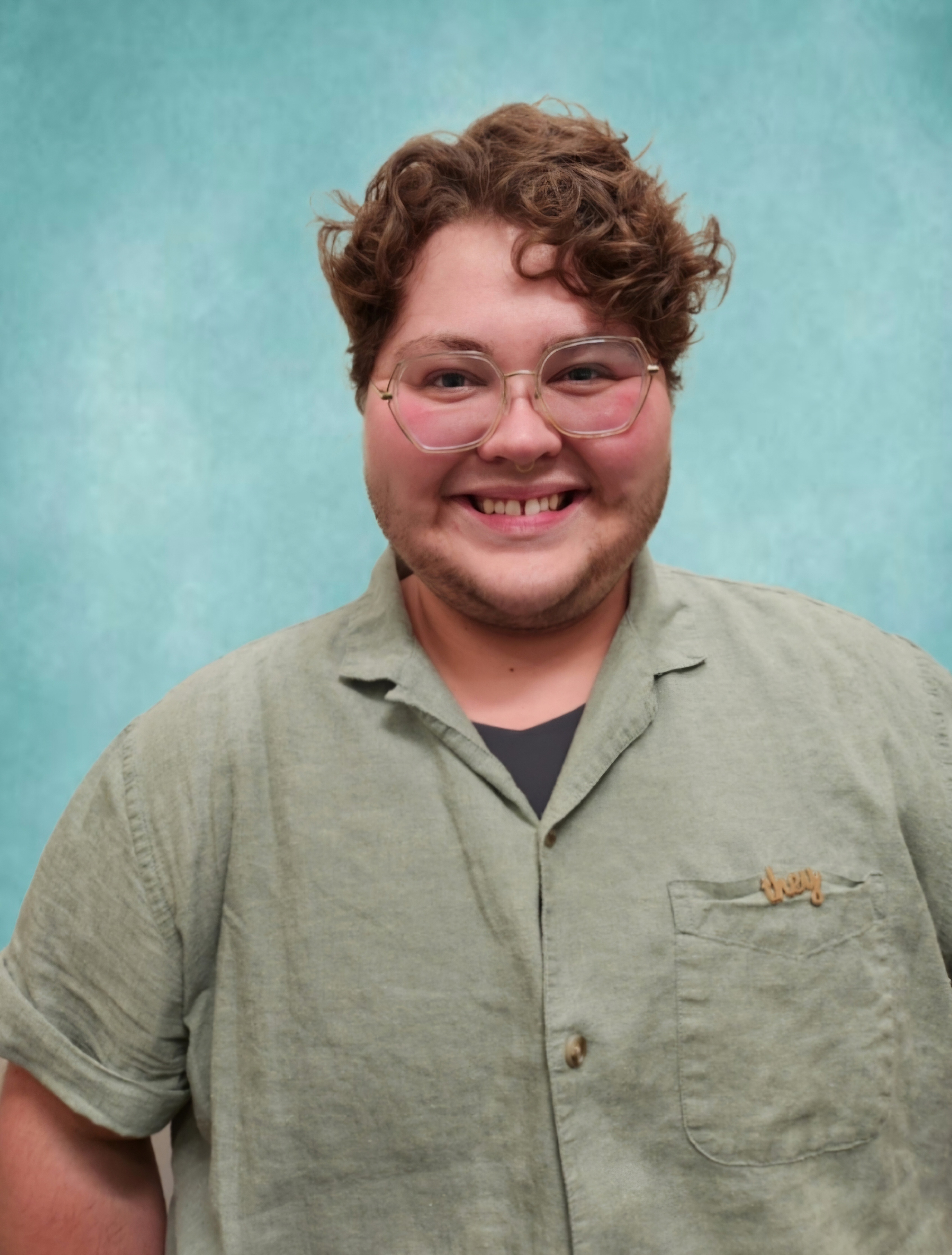 Knox smiles at the camera. They have short curly hair and large round glasses on.