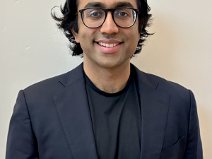 Vikram smiles at the camera while wearing a navy suit and black-rimmed glasses