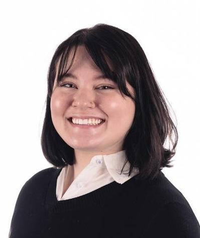 Macy, a young woman with a round face and shoulder-length dark hair, smiles at the viewer