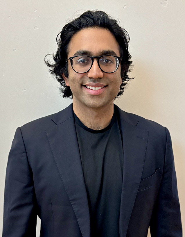 Vikram smiles at the camera while wearing a navy suit and black-rimmed glasses