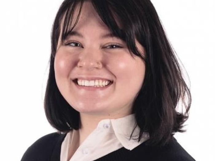 Macy, a young woman with a round face and shoulder-length dark hair, smiles at the viewer