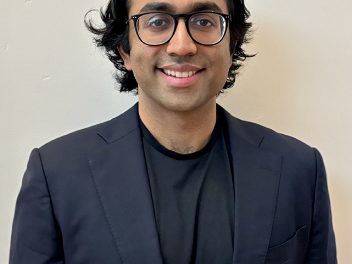 Vikram smiles at the camera while wearing a navy suit and black-rimmed glasses